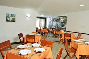 A dining area with tables set for four, wooden chairs, and orange tablecloths.