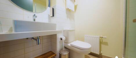 A bathroom with a white sink, mirror, toilet, and a small trash bin.