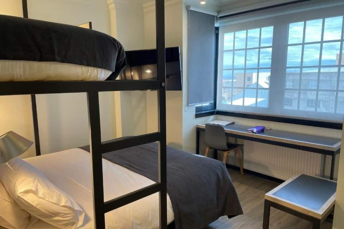 A bunk bed with a desk and chair, a small table, and a window with a view.