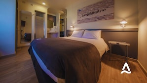 Una habitación de hotel con una cama grande, una mesita de noche, una lámpara de pared y un cuadro sobre la cama.