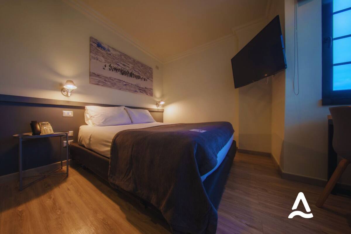A bedroom with a bed, bedside table, lamp, and a mounted TV.