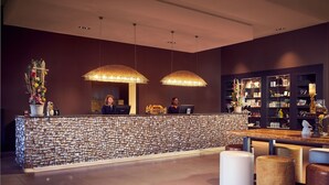 Un área de recepción con pared texturizada, dos lámparas colgantes grandes, un mostrador de recepción y una zona de estar con taburetes.