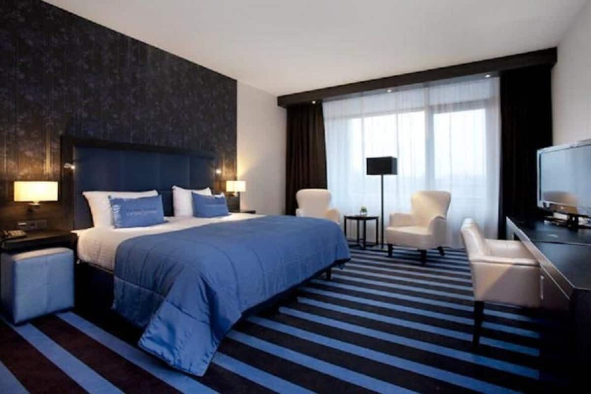 Una habitación de hotel moderna con una cama grande, un escritorio, una silla, un televisor y una lámpara.
