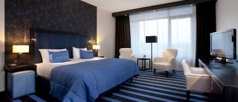 Una habitación de hotel moderna con una cama grande, un escritorio, una silla, un televisor y una lámpara.