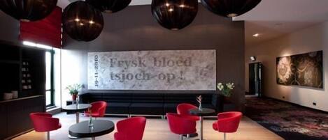 Un interior moderno con sillas rojas, una gran pantalla mural que muestra texto y lámparas de techo esféricas originales.