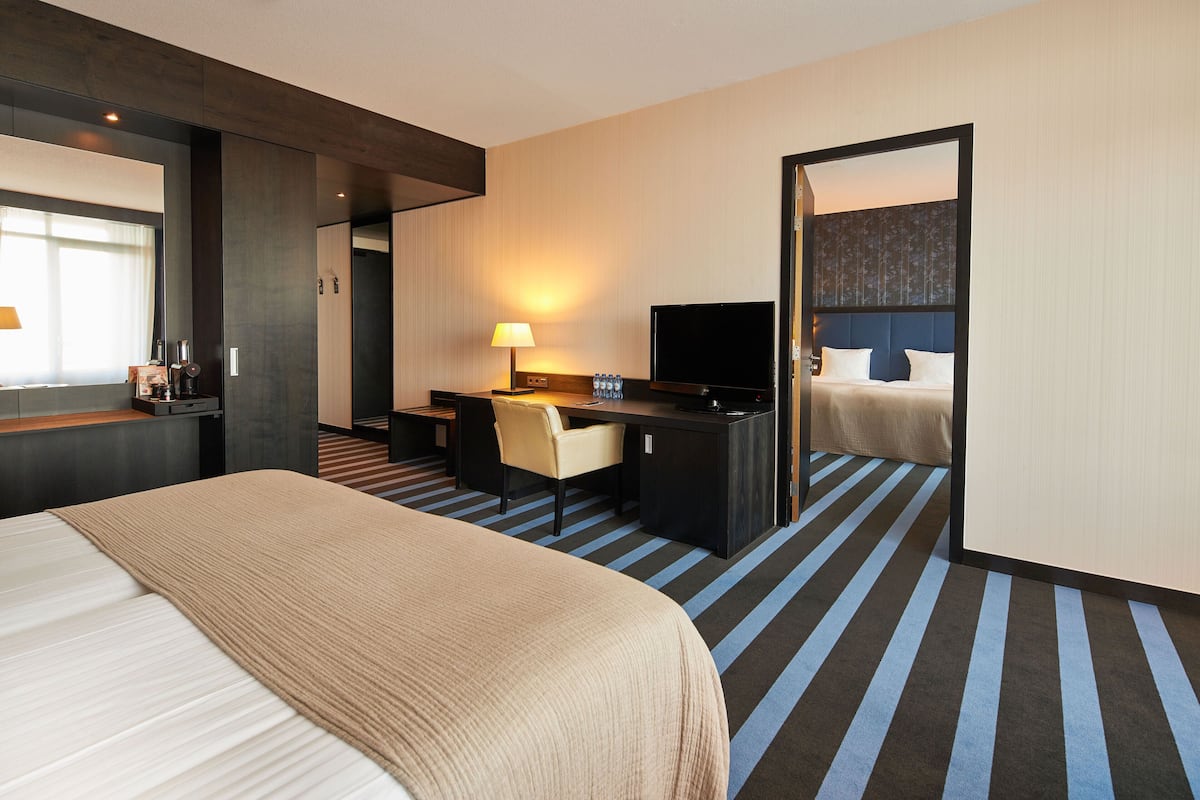 A hotel room with a large bed, a desk with a chair, a television, and a bathroom visible through an open door.