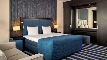 A hotel room with a large bed, two bedside tables with lamps, a chair, a small ottoman, and a large mirror.