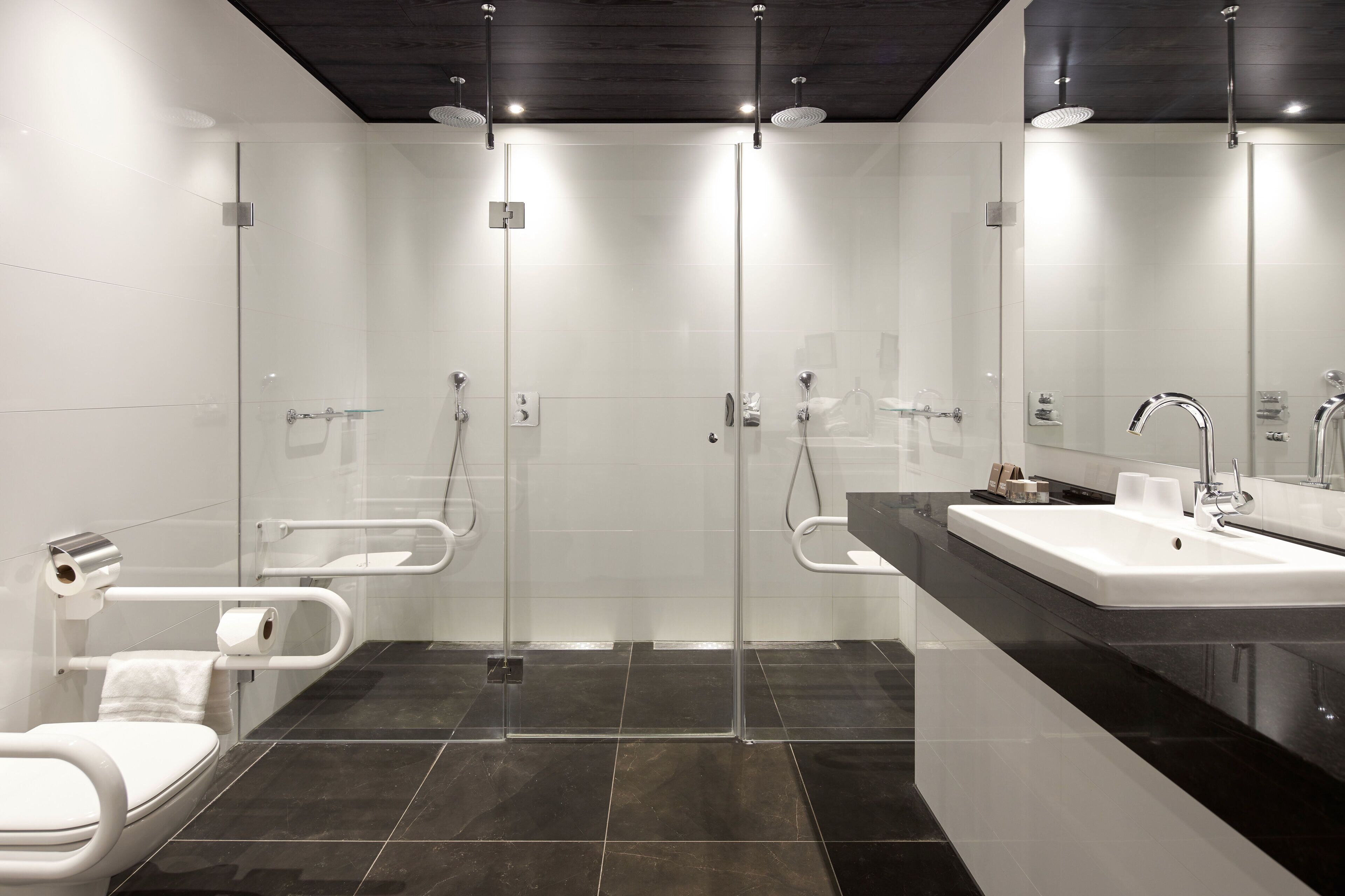 Un baño moderno con cabina de ducha de vidrio, inodoro blanco y encimera negra con lavabo.