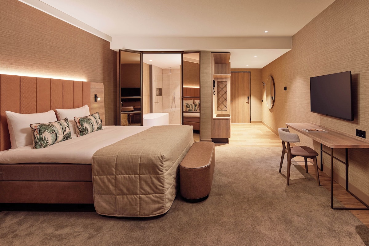 A modern hotel room with a large bed, a desk, and a TV.