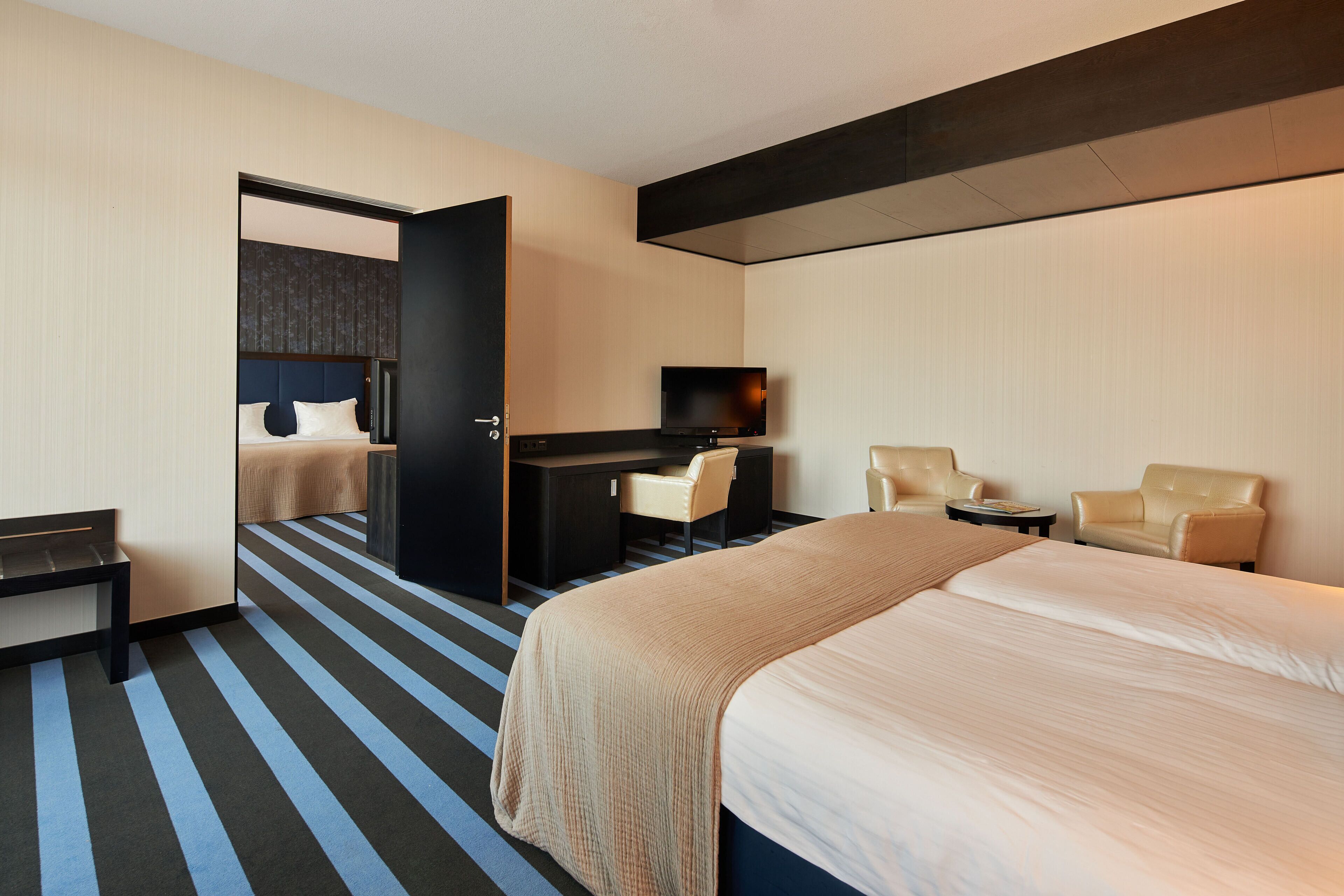 Una habitación de hotel con una cama grande, un escritorio con una silla, un televisor y dos sillones.