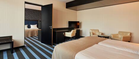 A hotel room with a large bed, a desk with a chair, a television, and two armchairs.