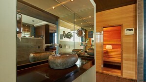 Un baño moderno con un espejo grande, dos lavamanos de granito y una sauna.