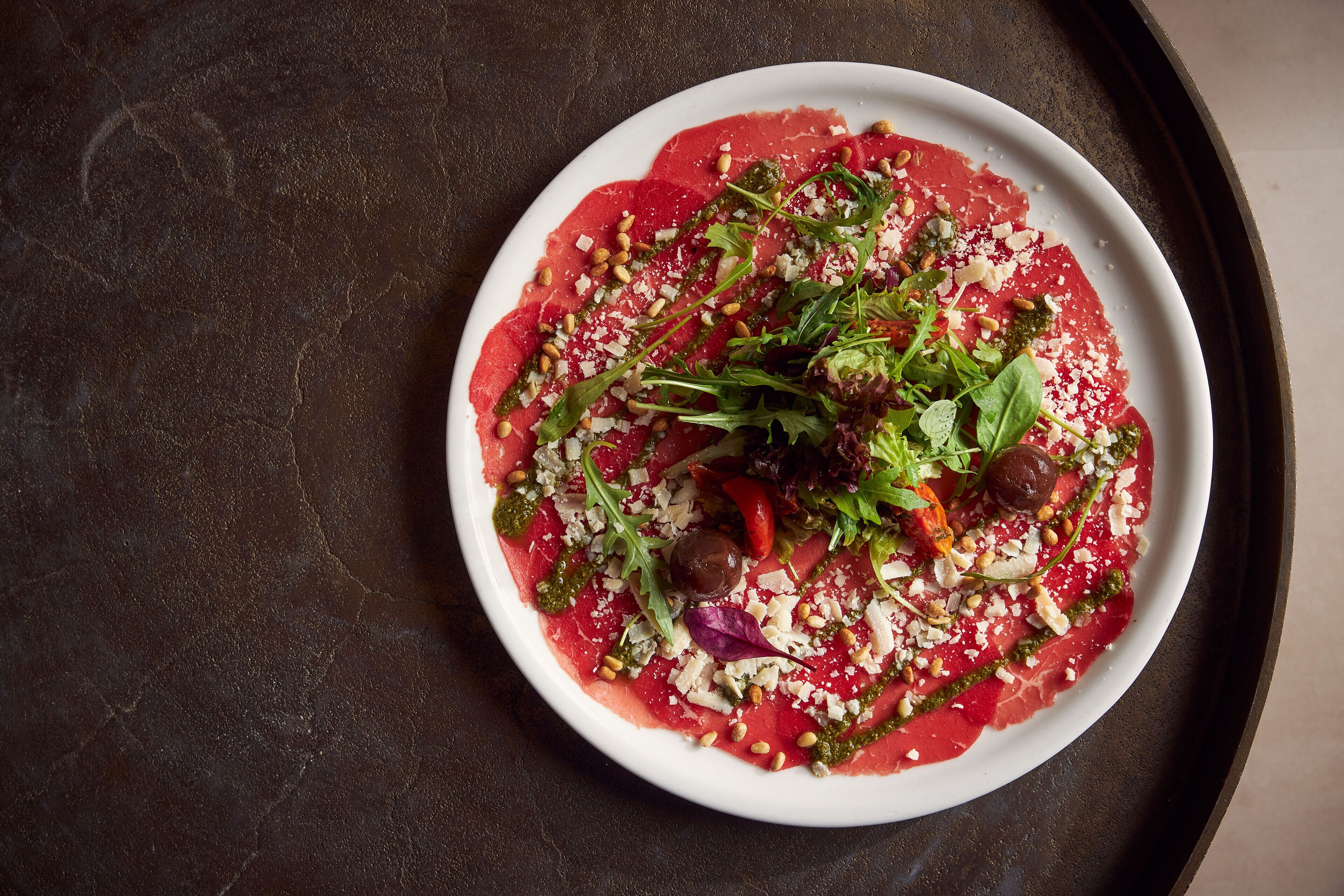 A plate of raw meat salad with various greens and nuts.