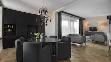 A modern living room with a round dining table, dark sofas, a chandelier, and a TV.