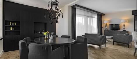 A modern living room with a round dining table, dark sofas, a chandelier, and a TV.