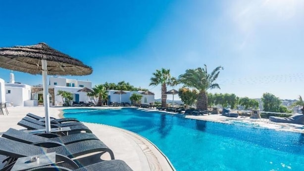 A poolside area with lounge chairs, a thatched umbrella, and white buildings in the background.