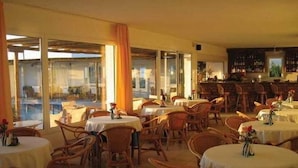 A restaurant with round tables and wicker chairs, large windows, and a bar area.