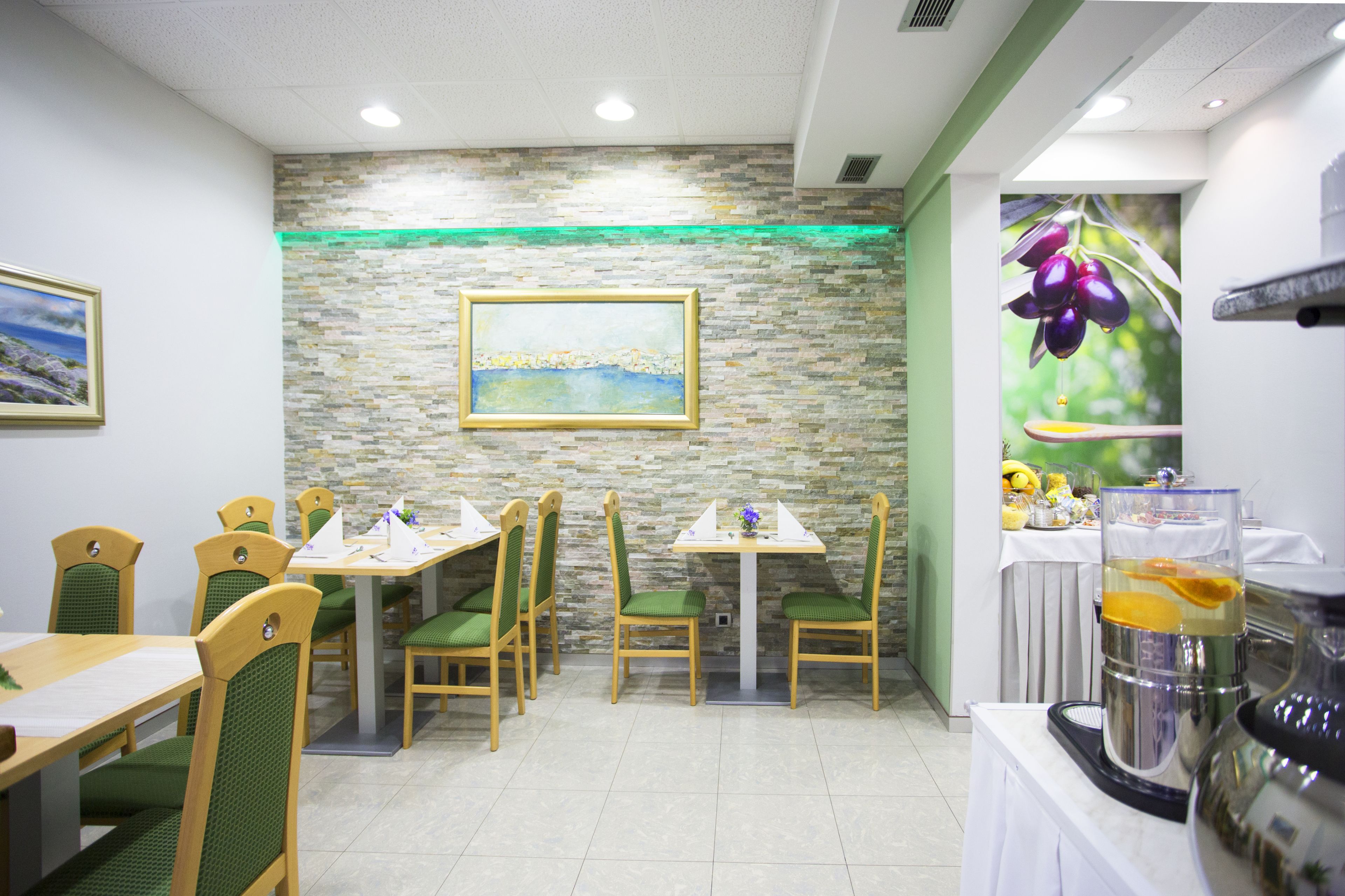 Un restaurante con pared de piedra, sillas verdes y una mesa con una jarra de jugo de naranja.
