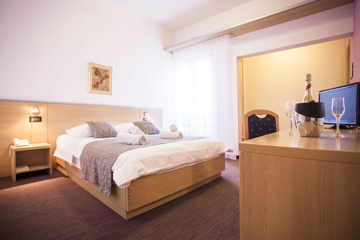 A hotel room with a bed, bedside table, lamp, and a television.