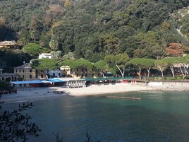 Una zona costiera con edifici, una spiaggia e un pendio boscoso.