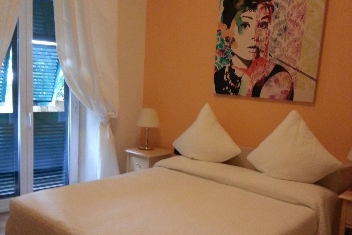Un dormitorio con cama, mesita de noche, lámpara y un cuadro en la pared.