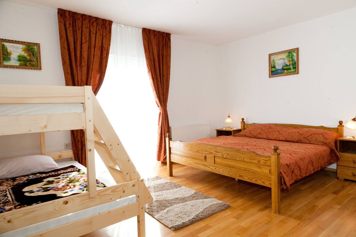 Un dormitorio con una cama alta, una cama individual, suelo de madera, una mesita de noche y dos lámparas fijadas a la pared.
