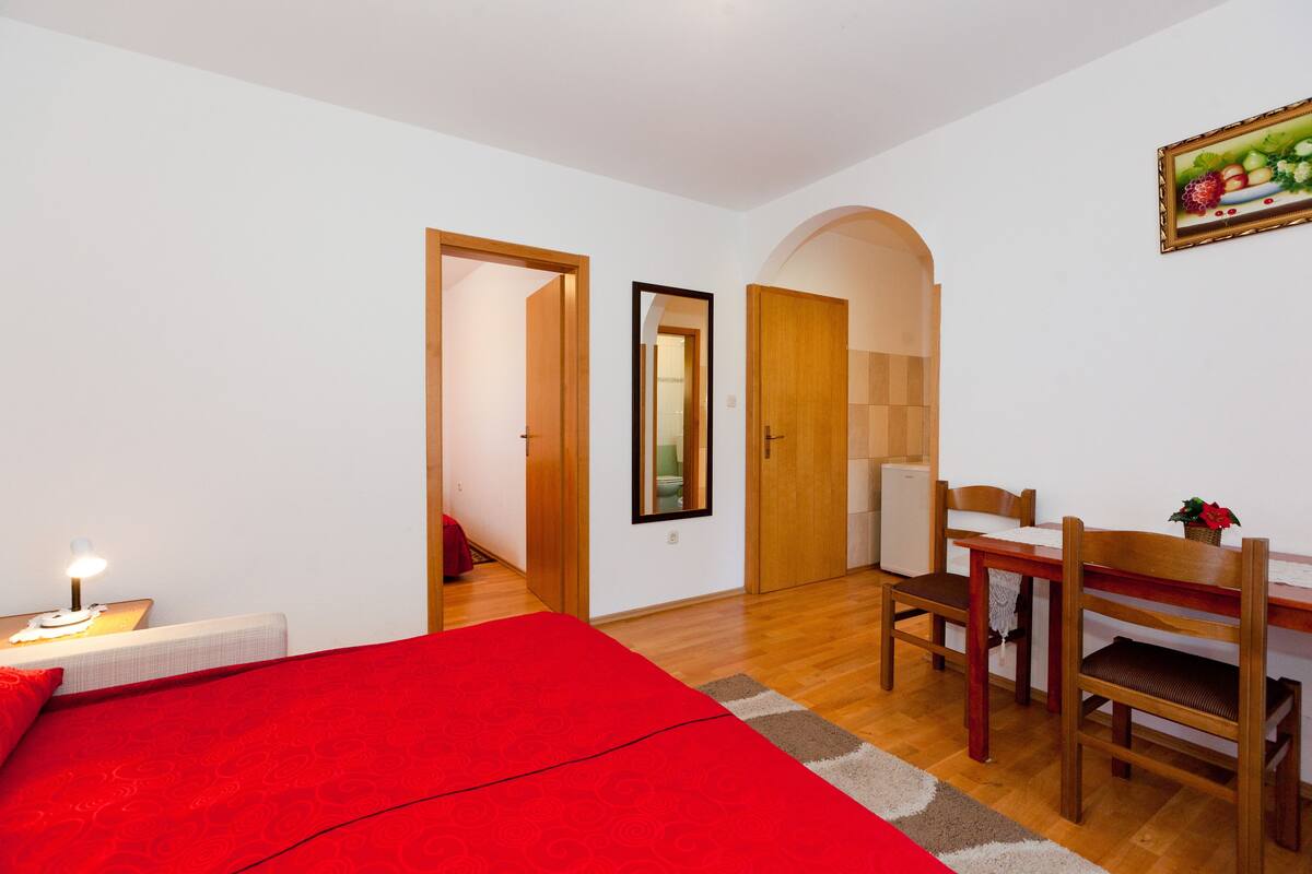 Un dormitorio con colcha roja, muebles de madera y una pequeña mesa con lámpara.