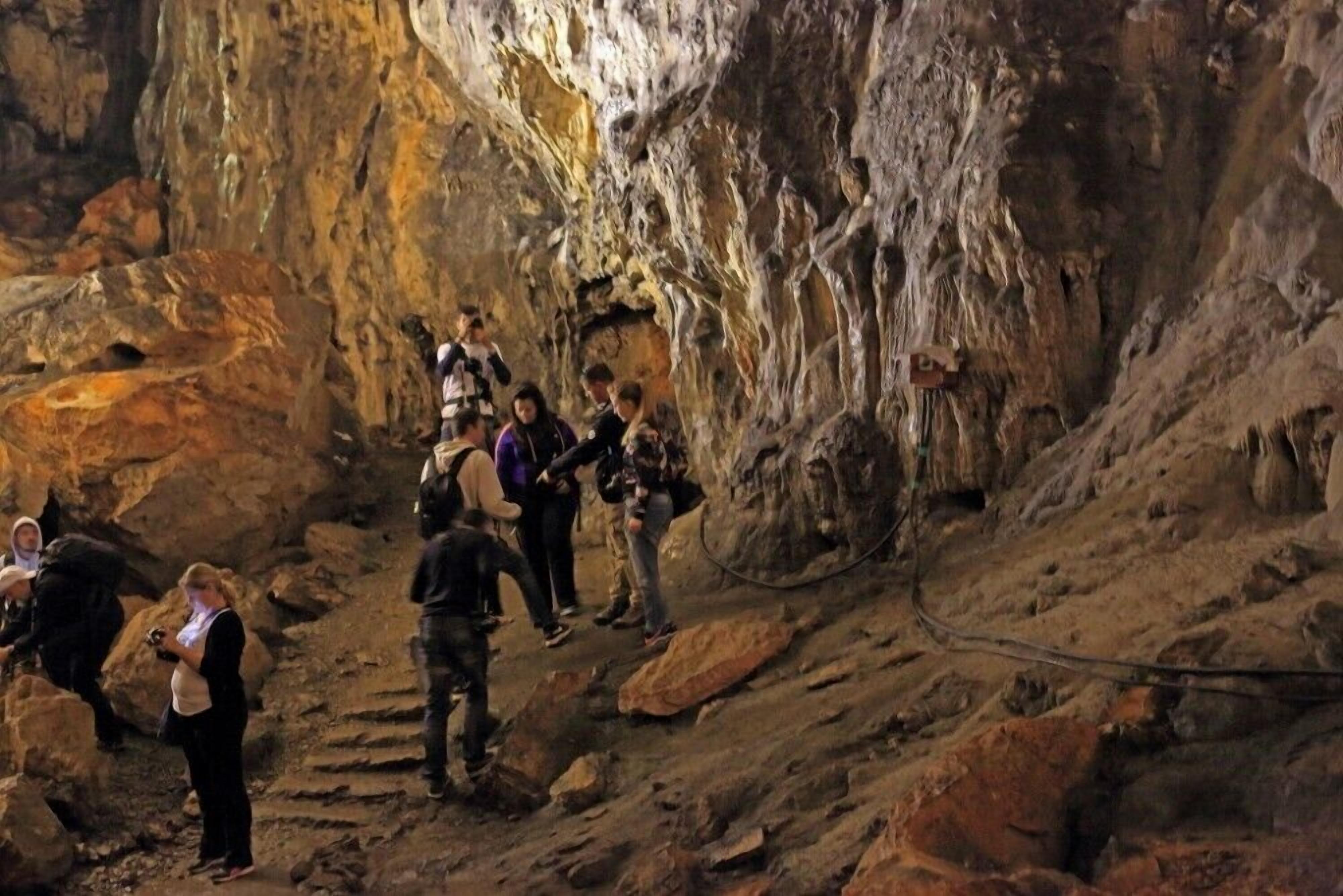 A group of people exploring a cave with rocky terrain and a rope for safety.