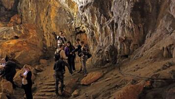 A group of people exploring a cave with rocky terrain and a rope for safety.