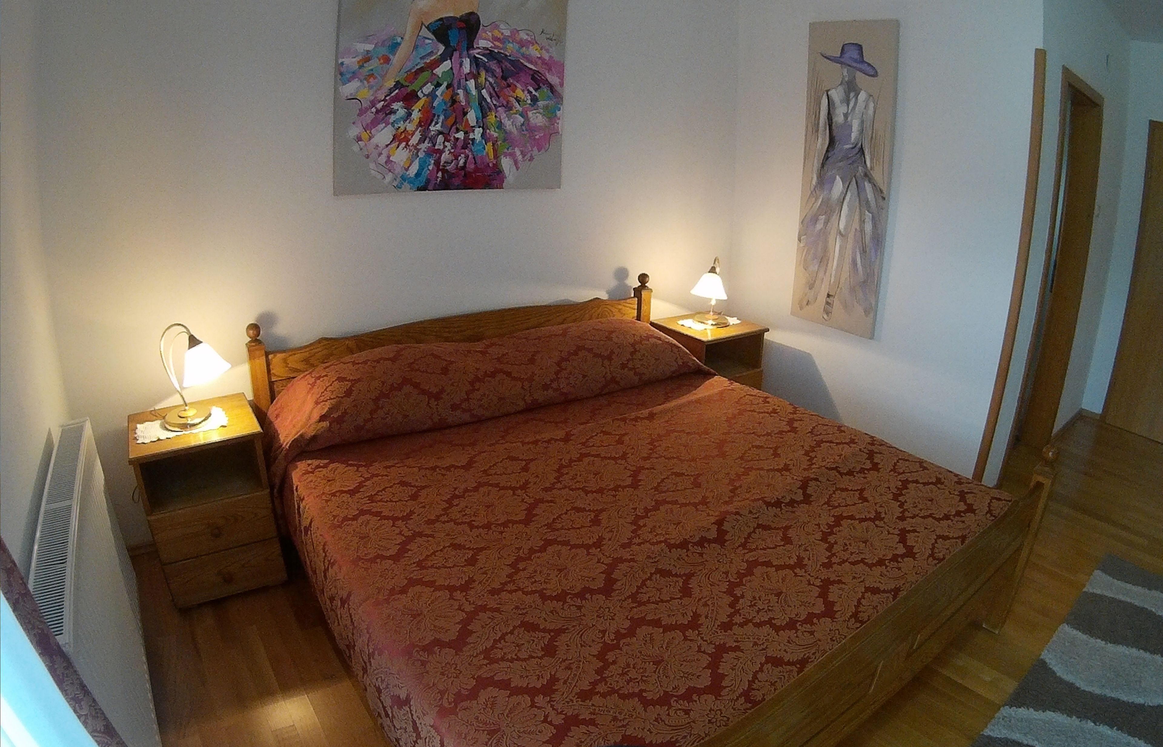Ein Schlafzimmer mit einem hölzernen Bett, zwei Nachttischen mit Lampen und zwei an der Wand befestigten Bildern.