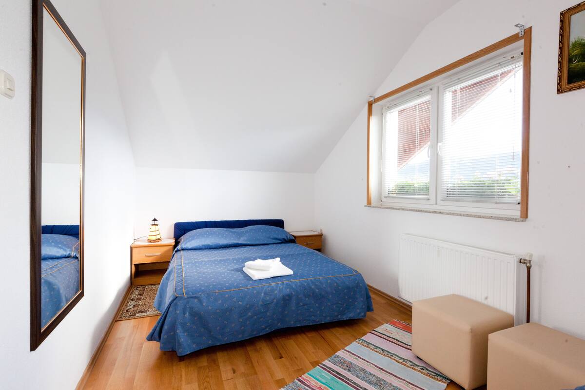Un dormitorio con cama, mesita de noche, lámpara, ventana con persianas y radiador.