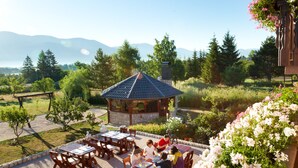 A gazebo with a tiled roof surrounded by a garden with flowers and trees, overlooking a mountainous landscape. - Pension Perisic (Plitvicka Jezera)