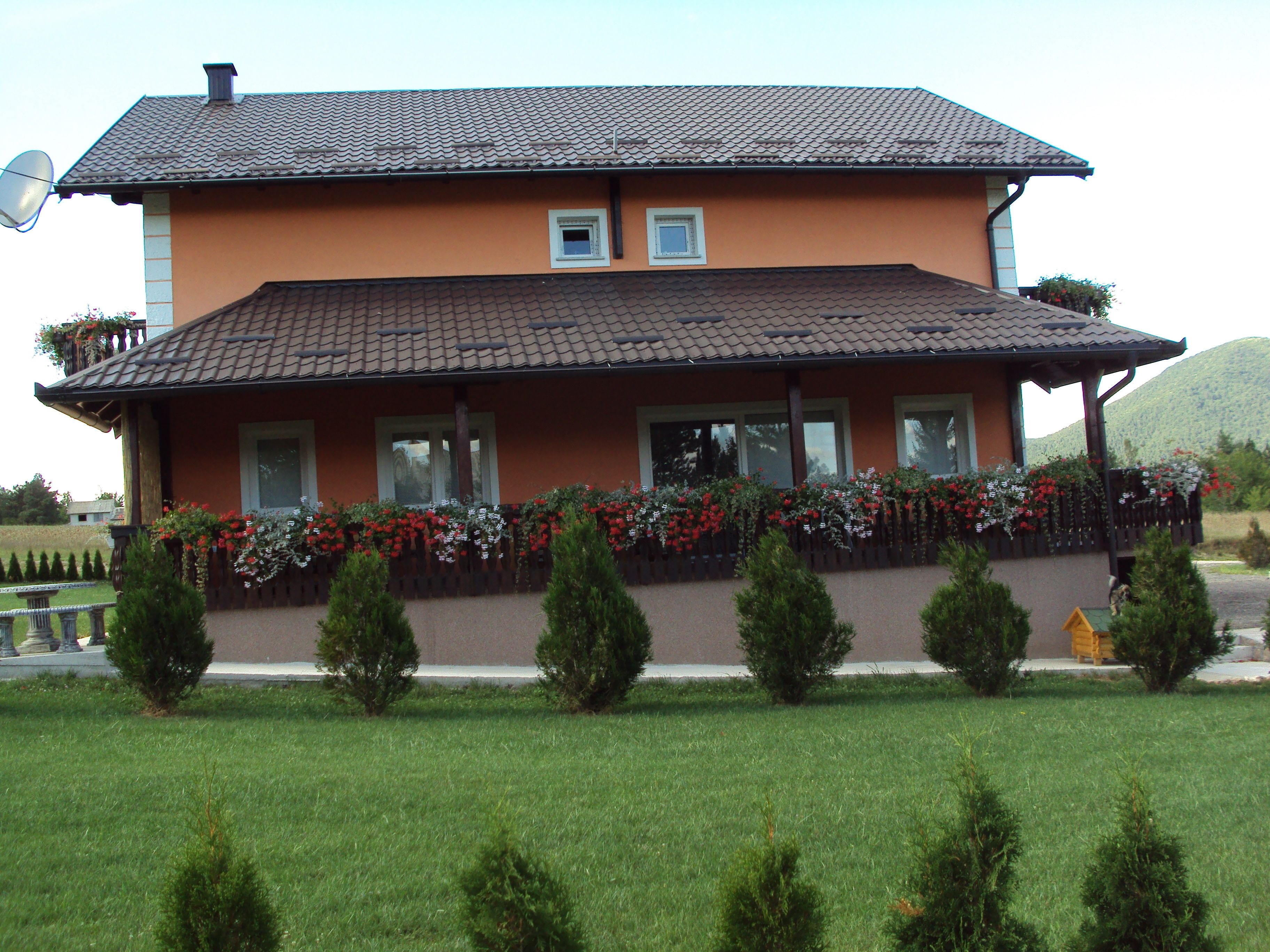 A two-story building with a tiled roof, a balcony with flower boxes, and a well-maintained lawn.