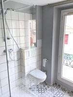 A bathroom with a shower, toilet, and a window with a view of buildings outside.