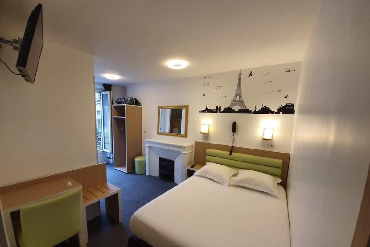 Habitación de hotel con cama, escritorio, silla, espejo, chimenea y un mural urbano en la pared.
