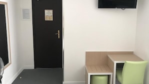 A small room with a black door, a white wall-mounted TV, a wooden table, and two green chairs. - Hôtel de La Herse d'Or (Paris)