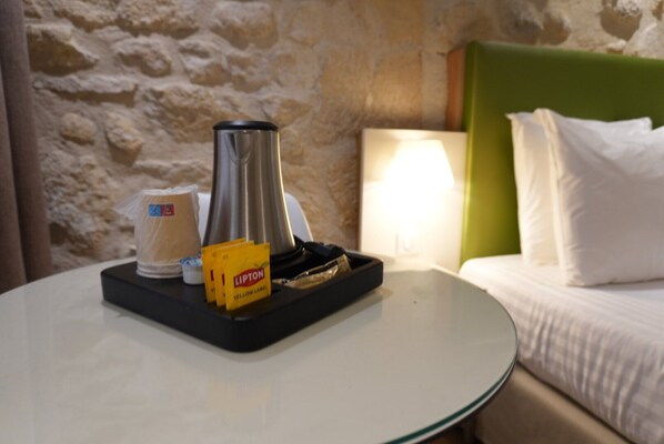 A hotel room with a bed, a nightstand, a lamp, a coffee maker, a cup, and a tray with Lipton tea bags. - Hôtel de La Herse d'Or (Paris)