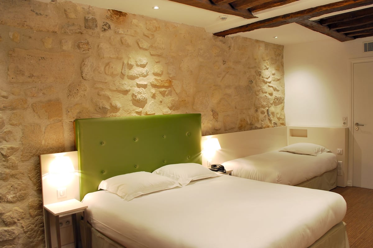 Una habitación con dos camas, una pared de piedra y un techo de madera.