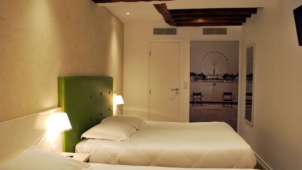 A hotel room with two beds, a green headboard, and a view of a Ferris wheel through an open door. - Hôtel de La Herse d'Or (Paris)