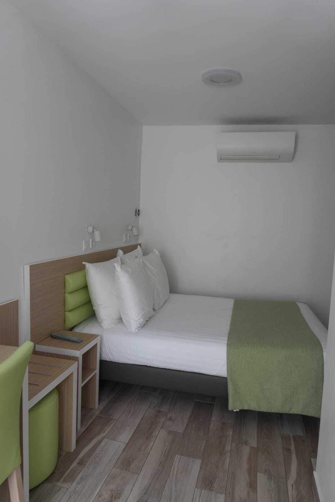 A compact hotel room with a single bed, a bedside table, a chair, and a small desk.