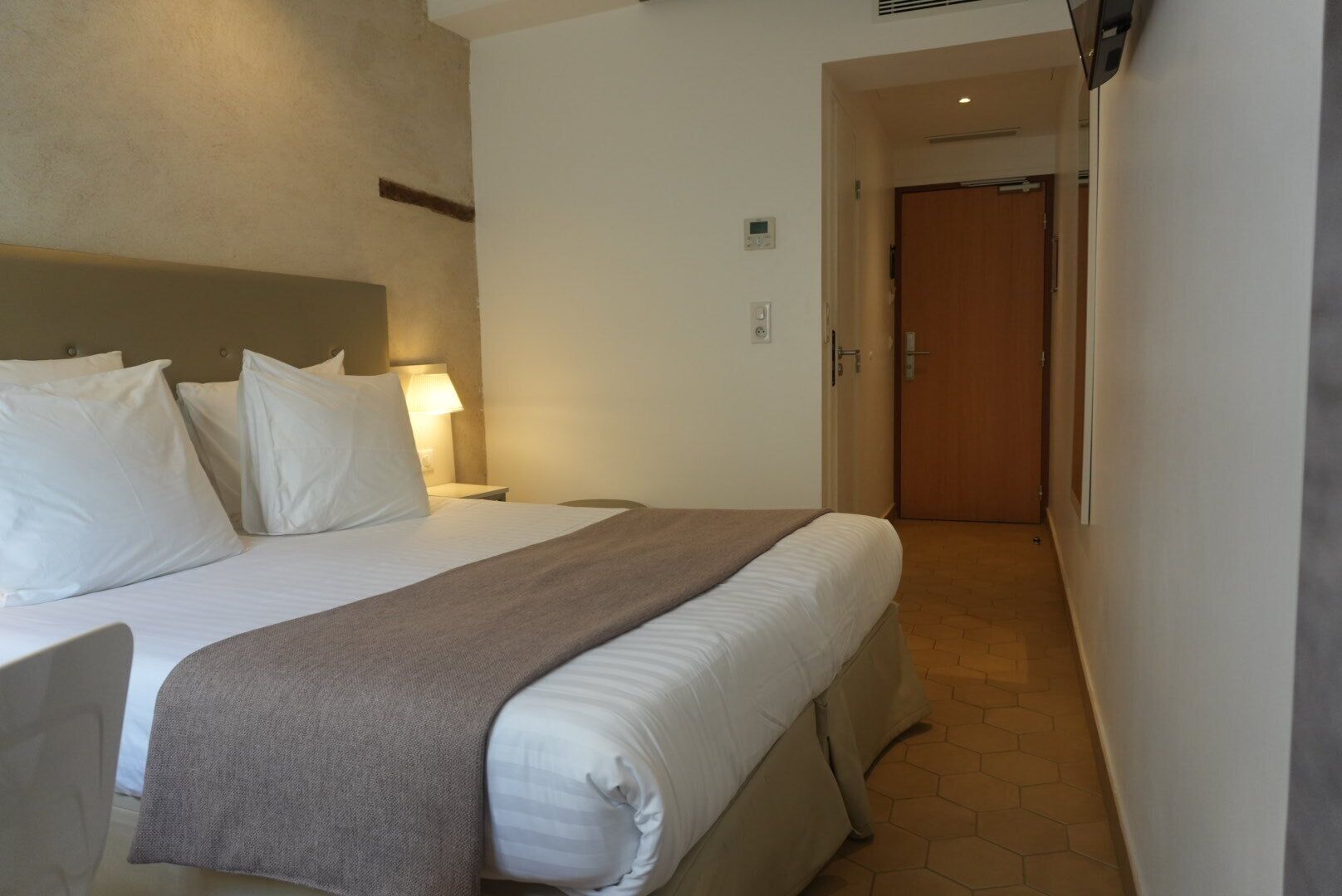 Habitación de hotel con cama, mesitas de noche, una lámpara y una puerta que da a otra habitación.