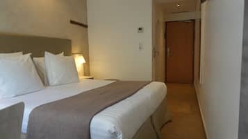 Habitación de hotel con cama, mesitas de noche, una lámpara y una puerta que da a otra habitación.