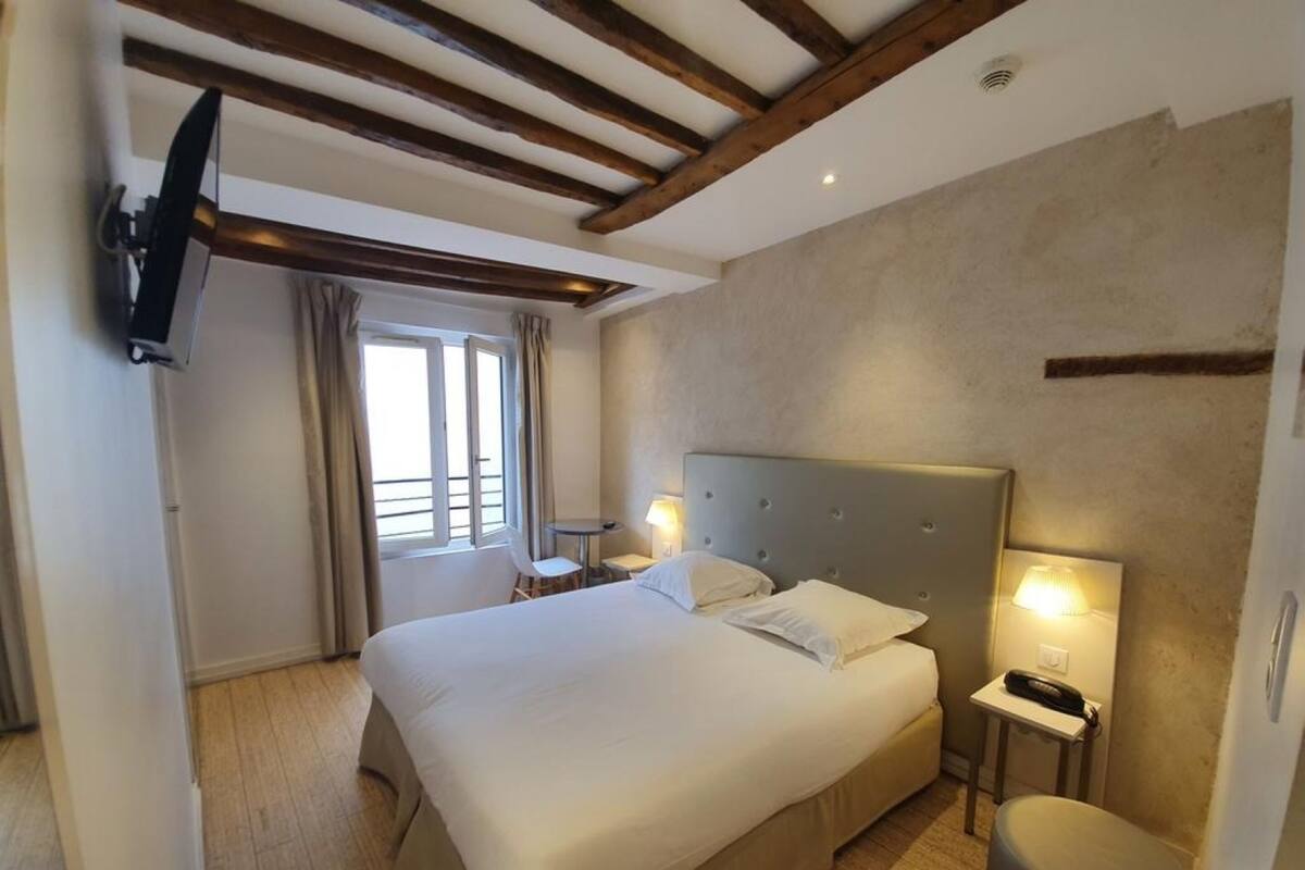 Una habitación de hotel con una cama grande, mesitas de noche con lámparas, un televisor montado en la pared y una ventana con cortinas.