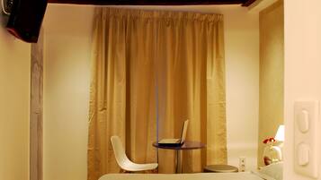 Quarto de hotel com cama, escrivaninha, cadeira, televisão e janela com cortinas.