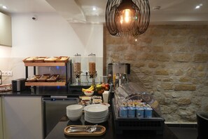 Mesa de desayuno buffet con pan, cereales, frutas y bebidas.