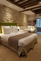 A hotel room with a stone wall, two beds with white bedding, a brown throw blanket, and a hexagonal floor pattern.