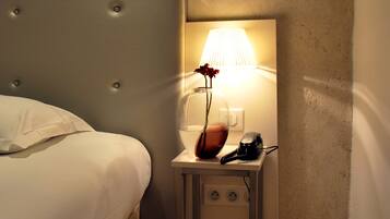 Una habitación de hotel con una cama, una mesita de noche con lámpara y un enchufe.