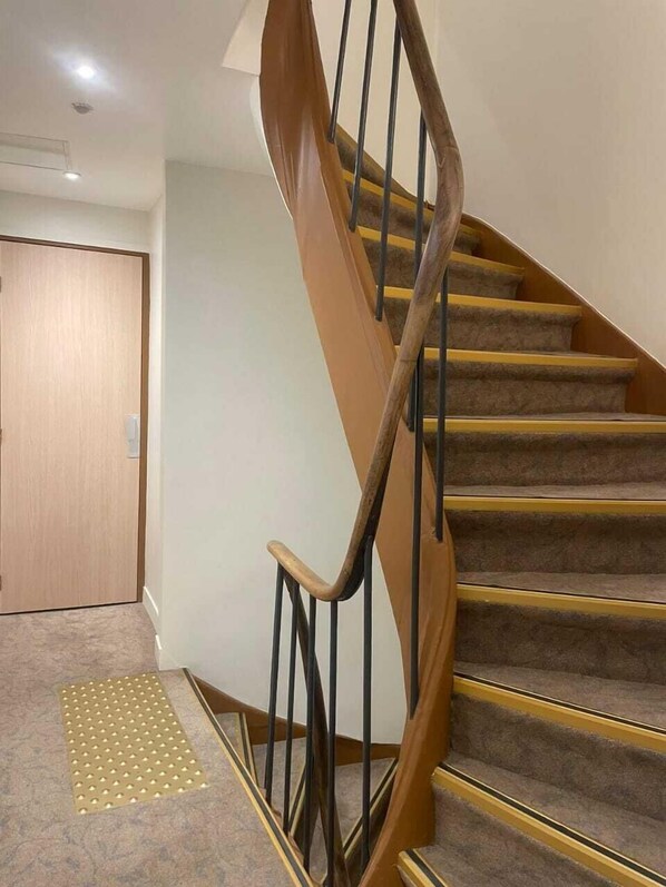 Una escalera con barandas de madera y peldaños alfombrados, que conduce a una puerta.