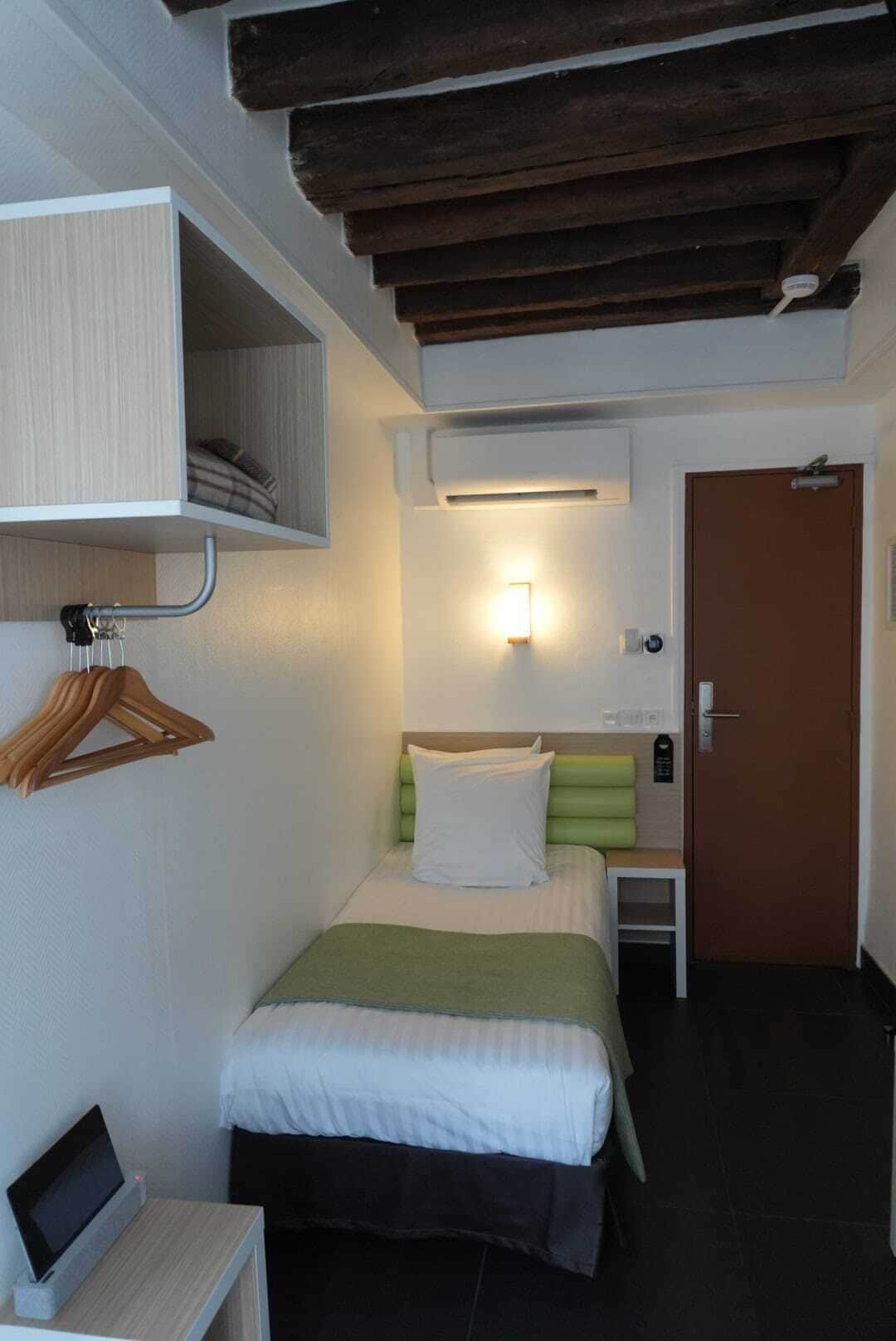 Habitación de hotel con cama, mesita de noche y aire acondicionado instalado en la pared.