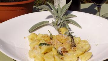 A plate of pasta with a garnish of sage and grated cheese, accompanied by a bottle of wine and a potted plant.